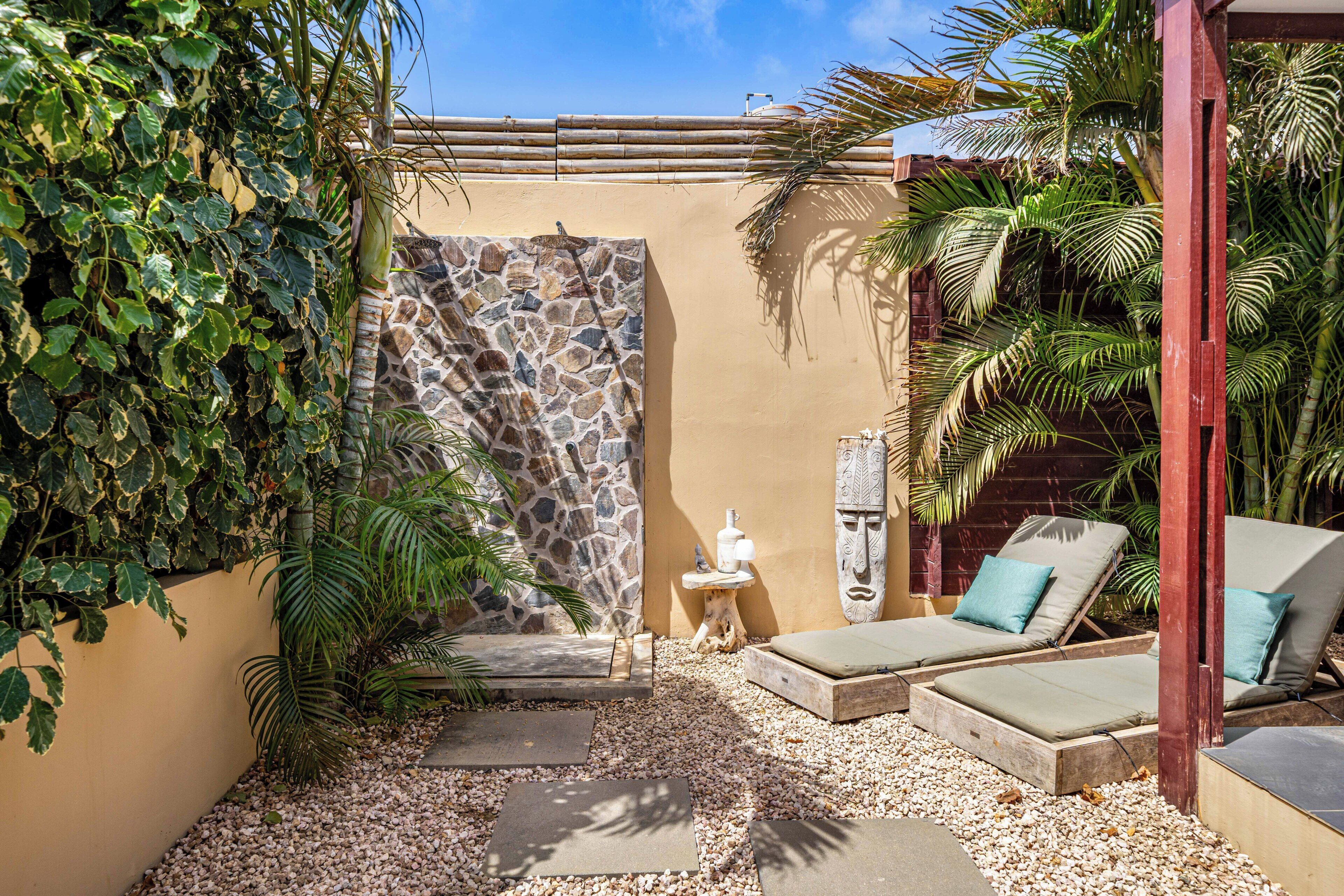 A private outdoor area with a stone wall, a small table with a vase, and two lounge chairs with cushions.