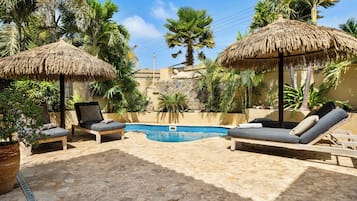 Una piscina al aire libre, sombrillas, sillones reclinables de piscina