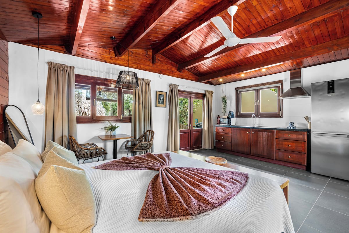 Un dormitorio con una cama grande, vigas de techo de madera, un comedor y una cocina con refrigerador.