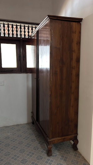 Een houten garderobe met spiegel, een raam met zonwering en een betegelde vloer.