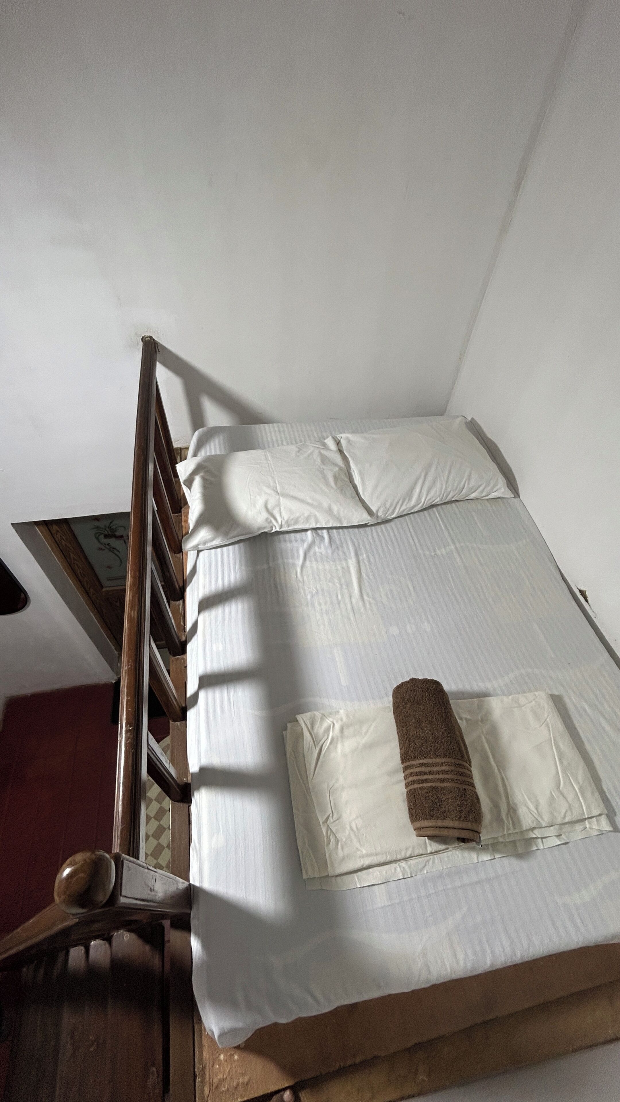 Een enkel bed met een houten hoofdbord, witte lakens en een bruine handdoek.