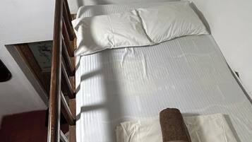 Een enkel bed met een houten hoofdbord, witte lakens en een bruine handdoek.