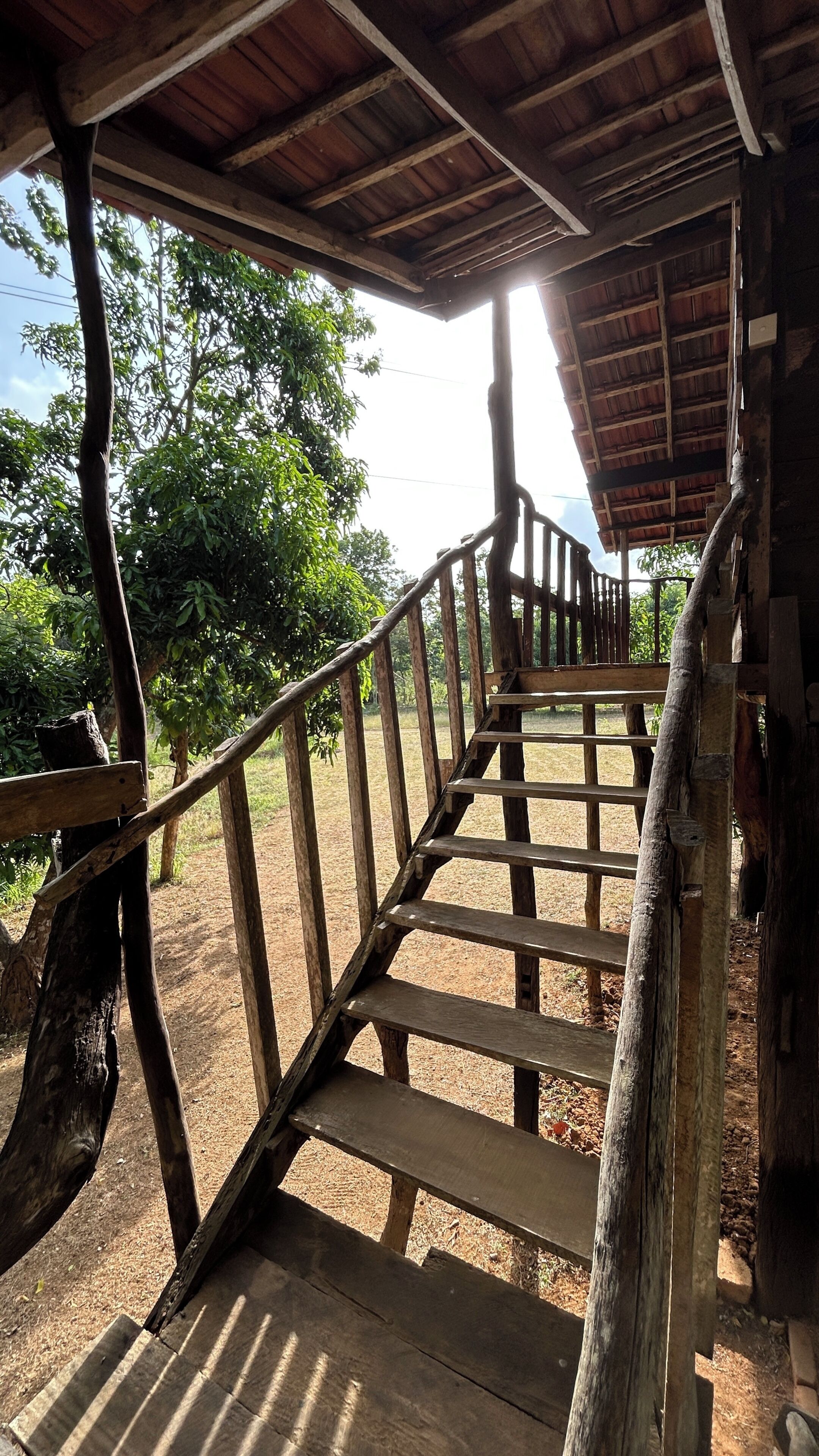 A wooden staircase leading to a covered area with a view of trees and a clear sky.