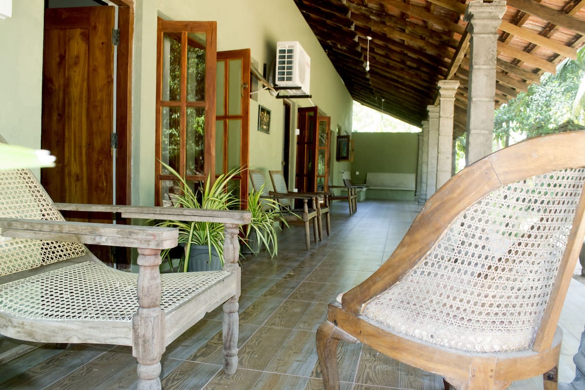 A covered outdoor seating area with wooden chairs and tables, potted plants, and wooden doors.