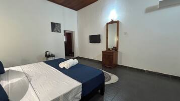Quarto de hotel com cama, mesa de cabeceira com chaleira, espelho e televisão na parede.