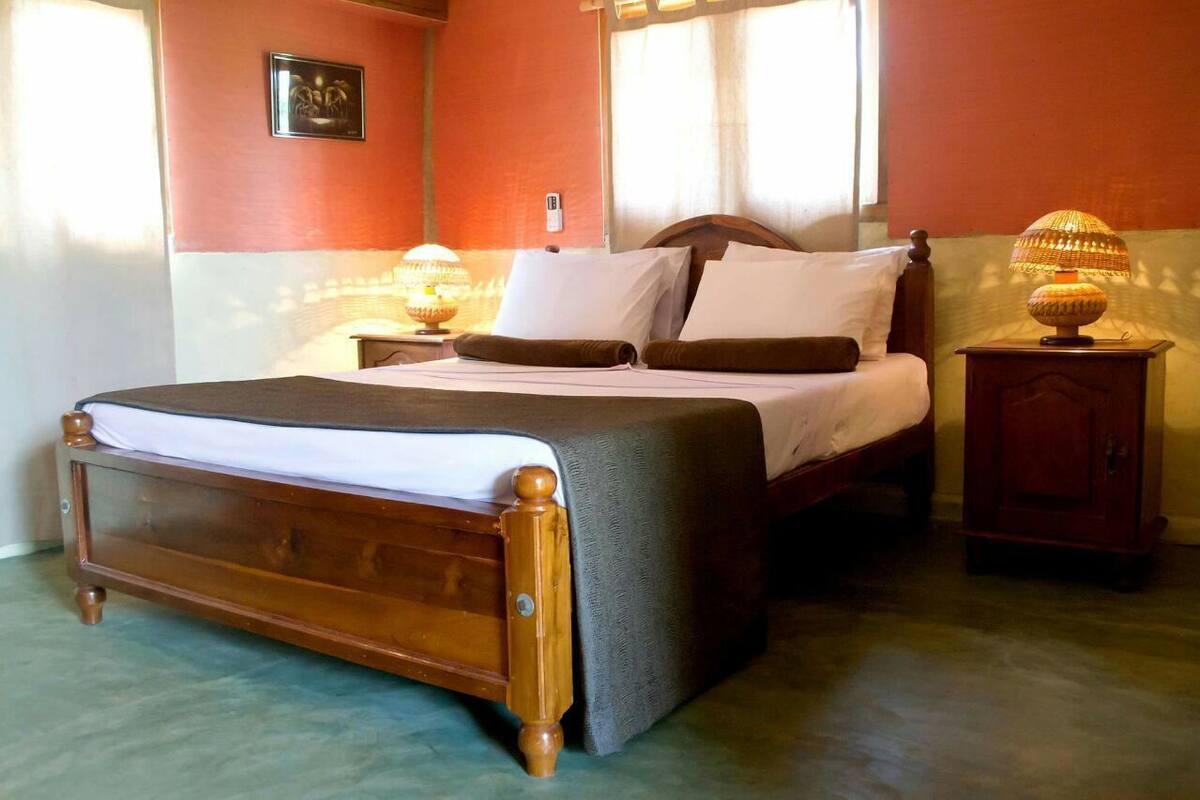 A neatly made bed with a wooden frame and a grey bedspread, two bedside lamps, and a small wooden nightstand with a lamp.