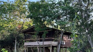 A rustic wooden structure with a balcony, surrounded by dense greenery and trees.