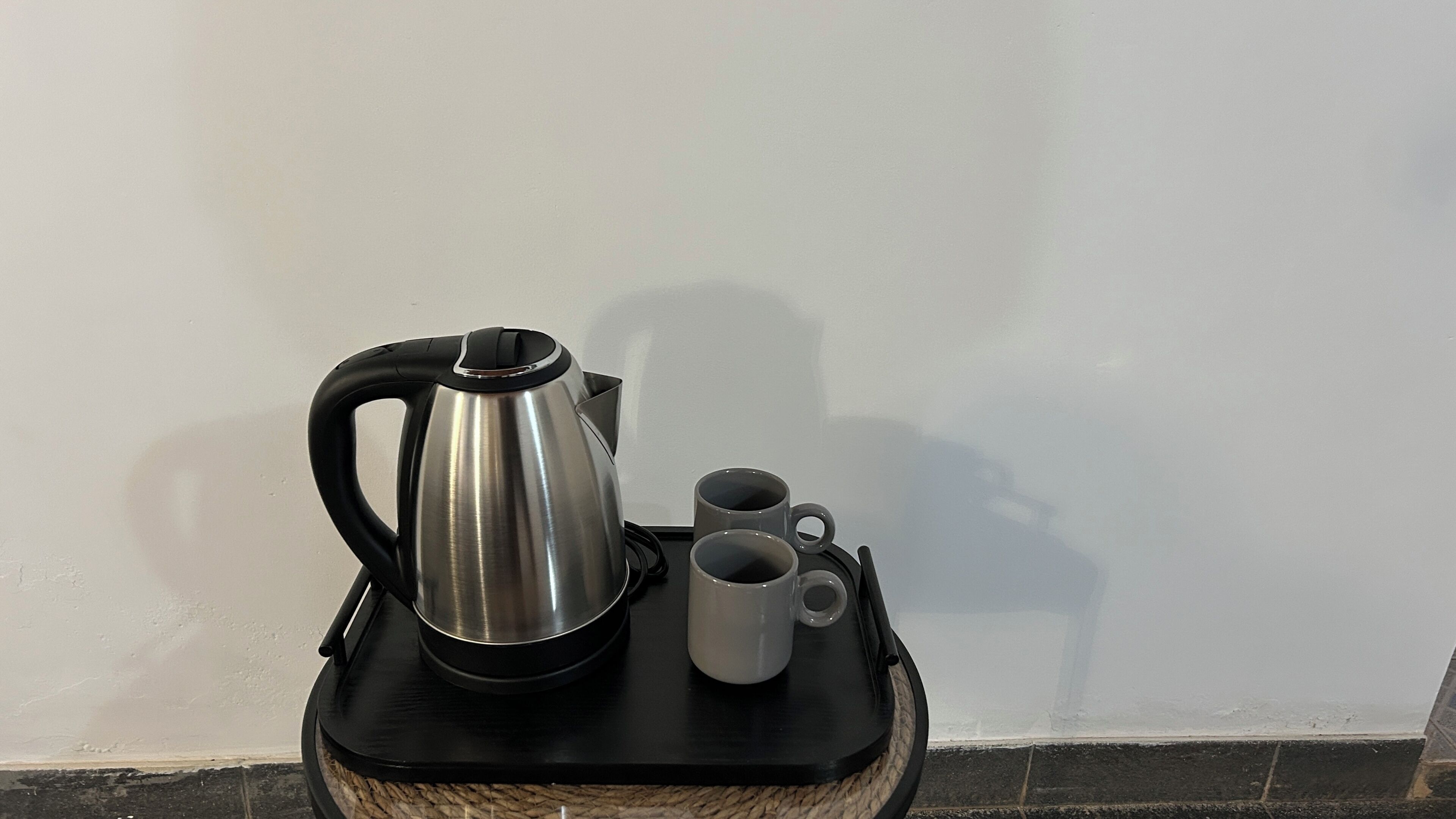 Una tetera de acero inoxidable y dos tazas sobre una bandeja negra.