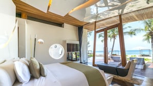 A modern bedroom with a large bed, a circular mirror, and a view of the beach. - Iniala Beach House (Takua Thung)