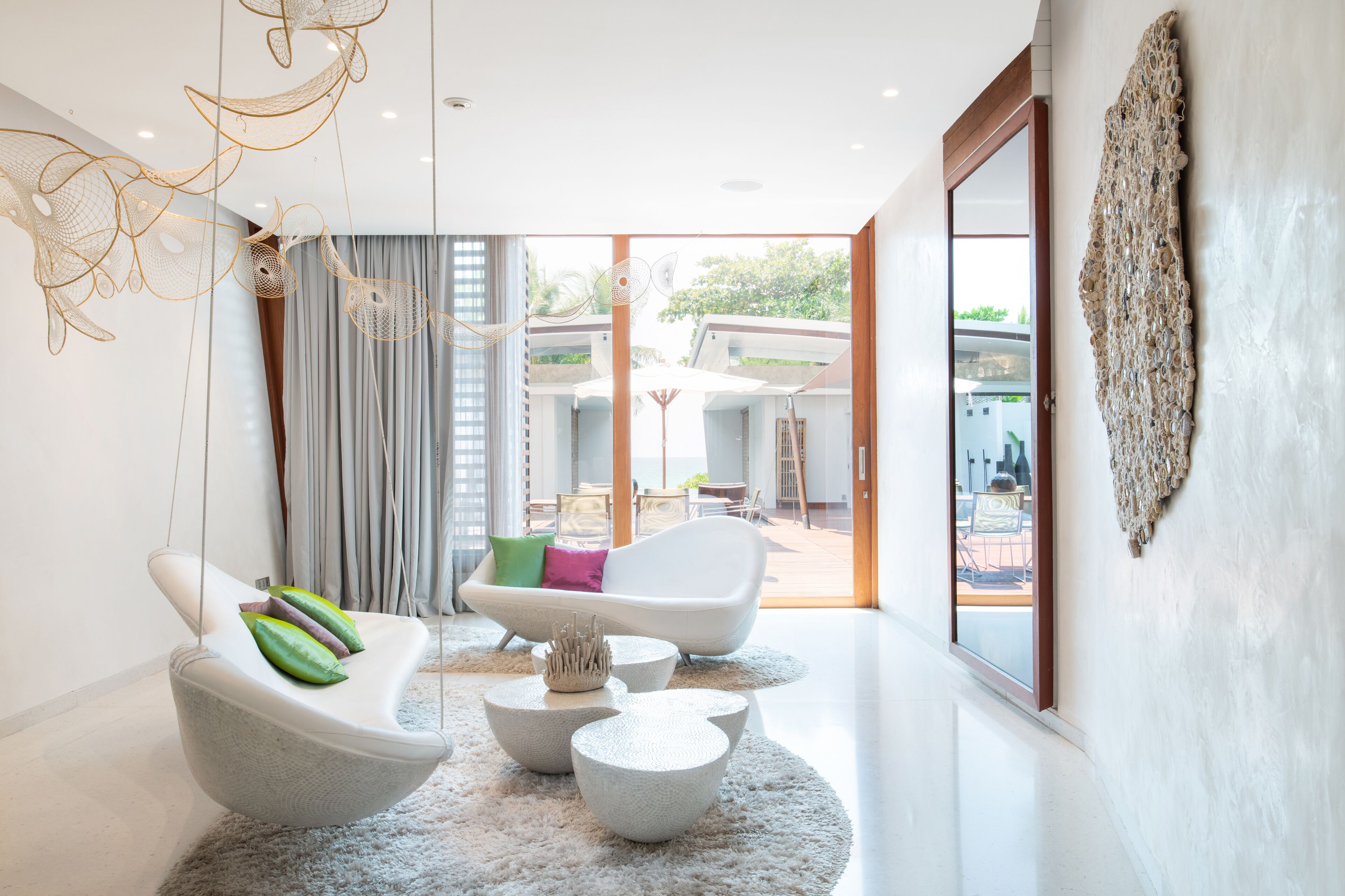 Un salón moderno con un sofá blanco, un sillón blanco y una mesa de centro. Hay un ventanal con vistas al exterior.