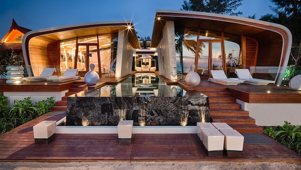 A modern resort with a central pool, wooden deck seating, and a stone waterfall feature. - Iniala Beach House (Takua Thung)