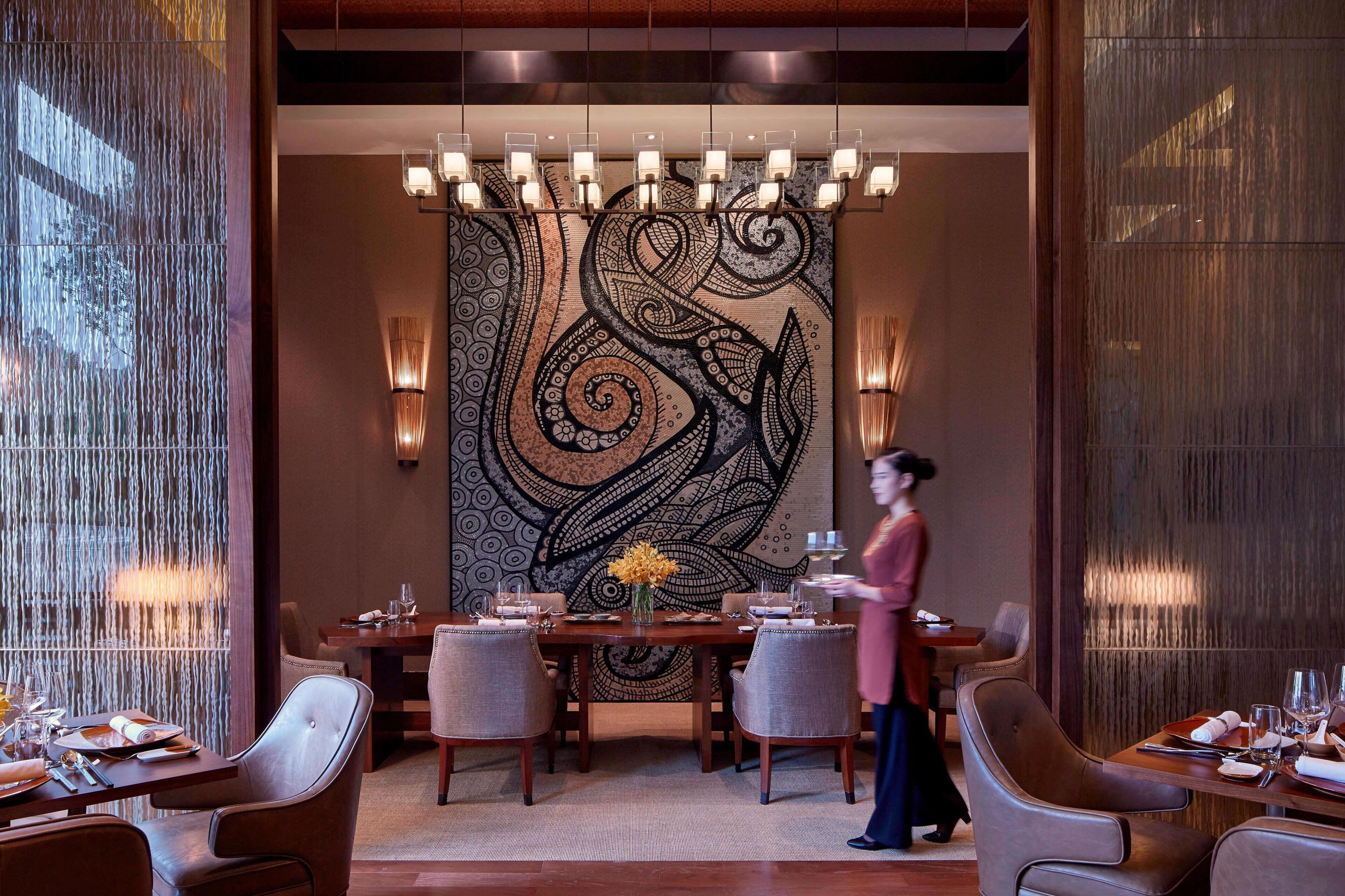 A dining area with a large wall tapestry, multiple dining tables, and ambient lighting.
