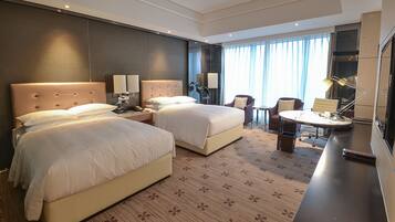 Ein Hotelzimmer mit zwei Betten, einem Schreibtisch, einem Stuhl und einem kleinen Tisch.