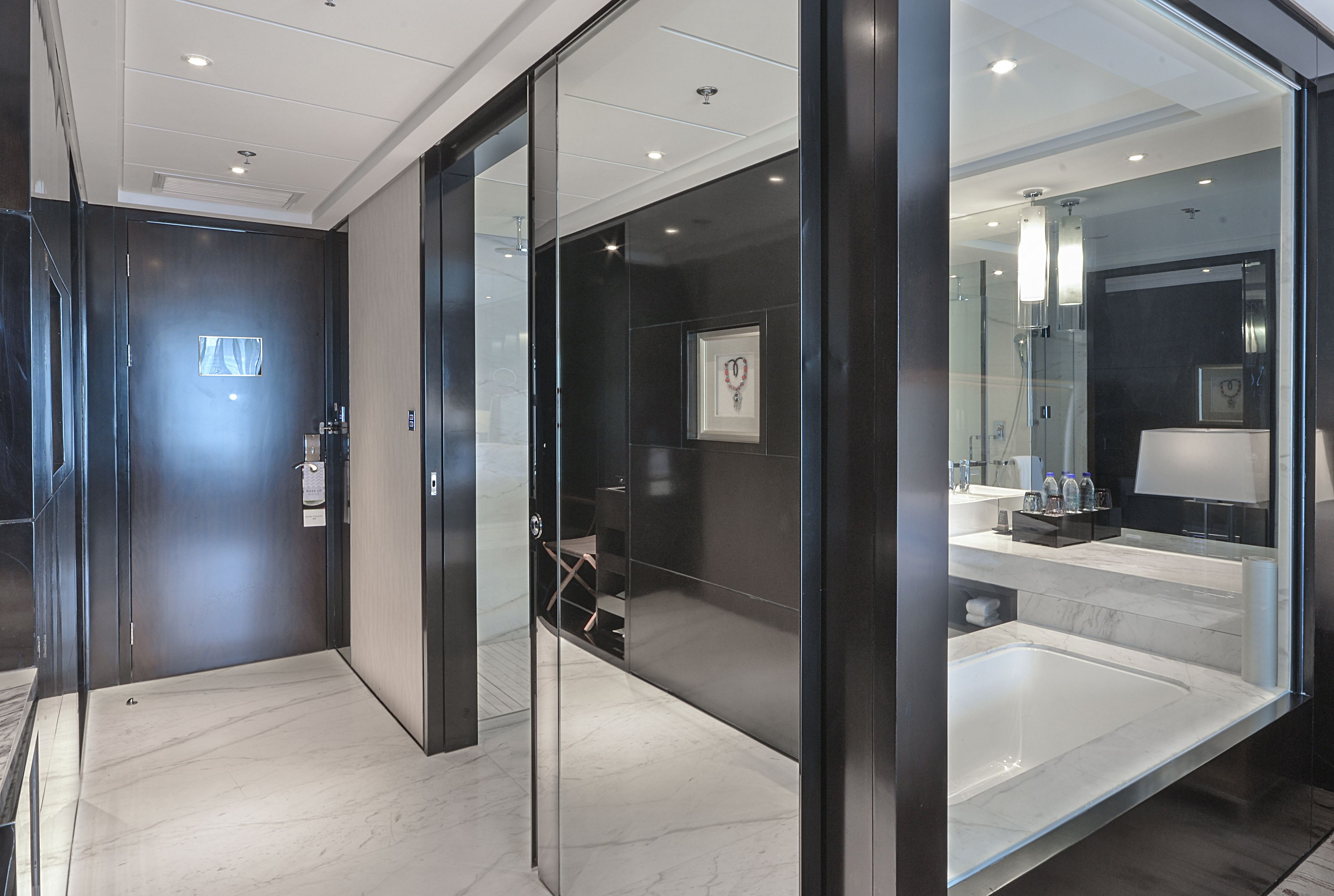 Un moderno vestíbulo de hotel con un separador de vidrio, una mesa de recepción y un baño a la vista con una bañera grande y tocador.