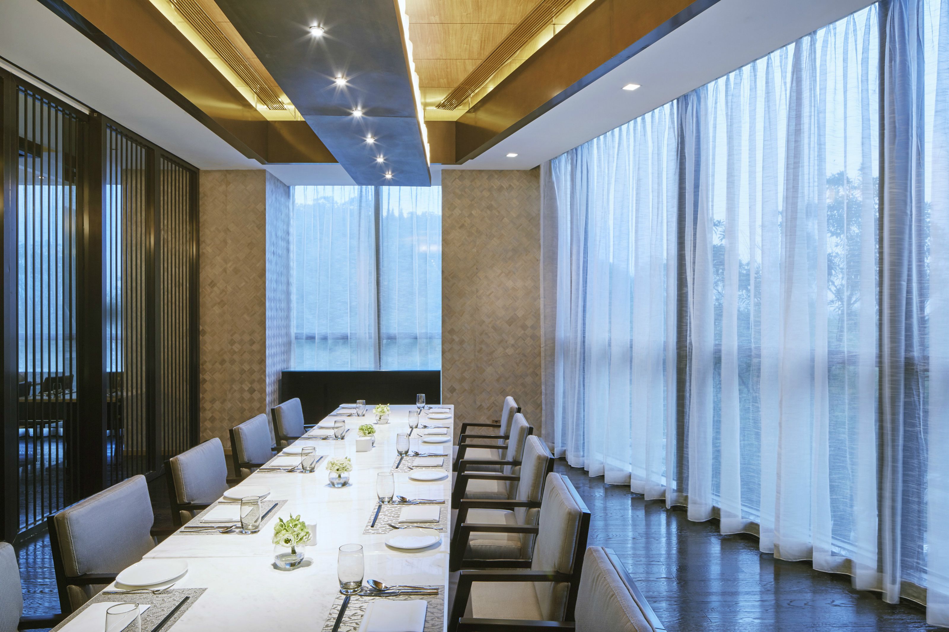 A conference room with a long table, chairs, and large windows with sheer curtains.
