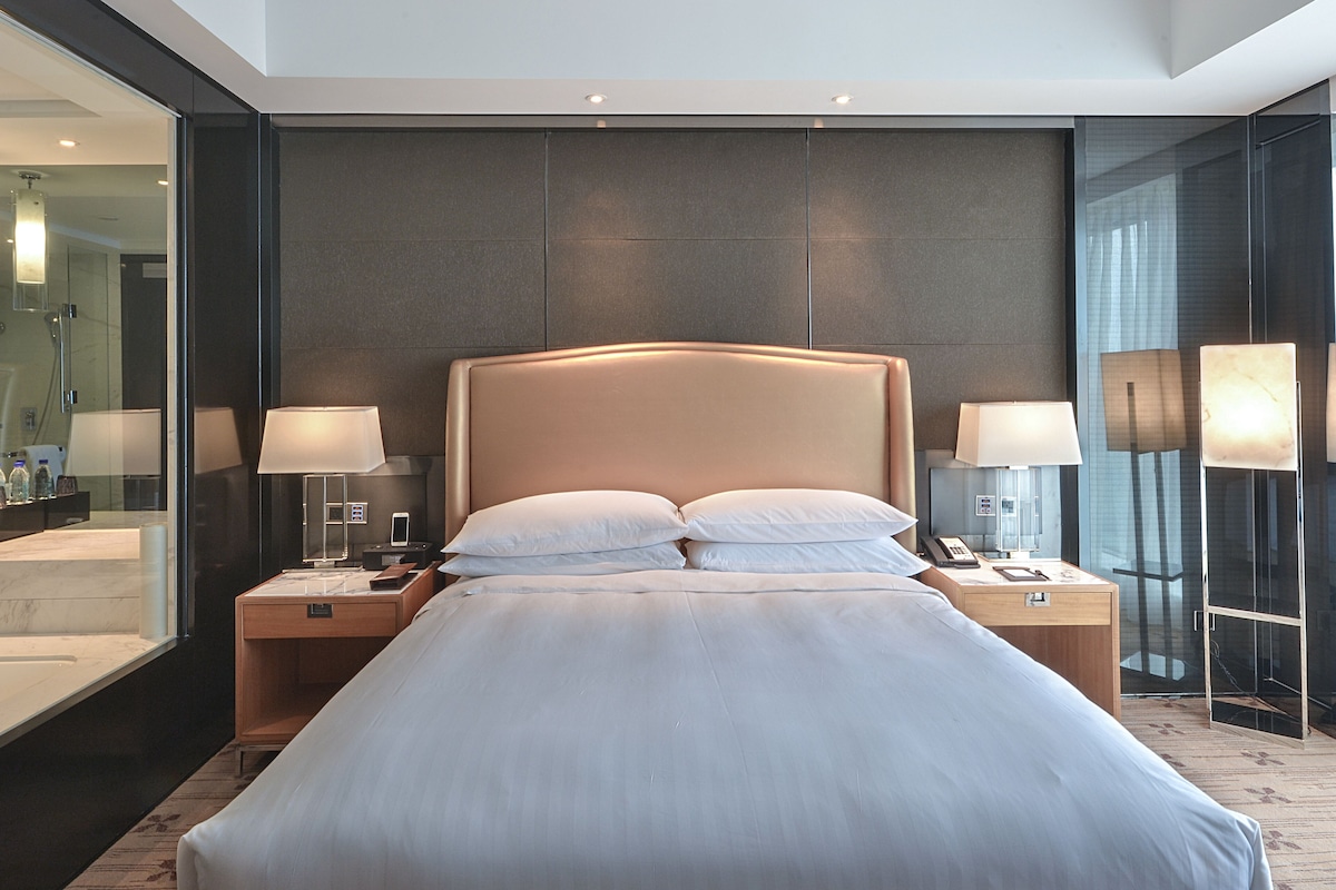 Une chambre d’hôtel moderne avec un grand lit, des lampes de chevet, une table de chevet et une douche en verre.