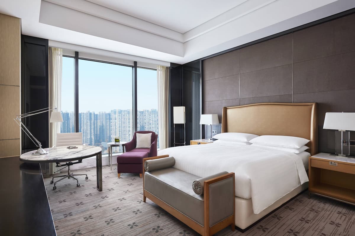 Habitación de hotel con una cama grande, un escritorio, una silla y vistas de la ciudad.