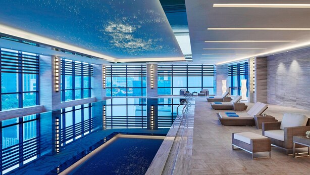 Ein moderner Poolbereich im Innenbereich mit großen Fenstern, Liegestühlen und einem zentral gelegenen Pool.
