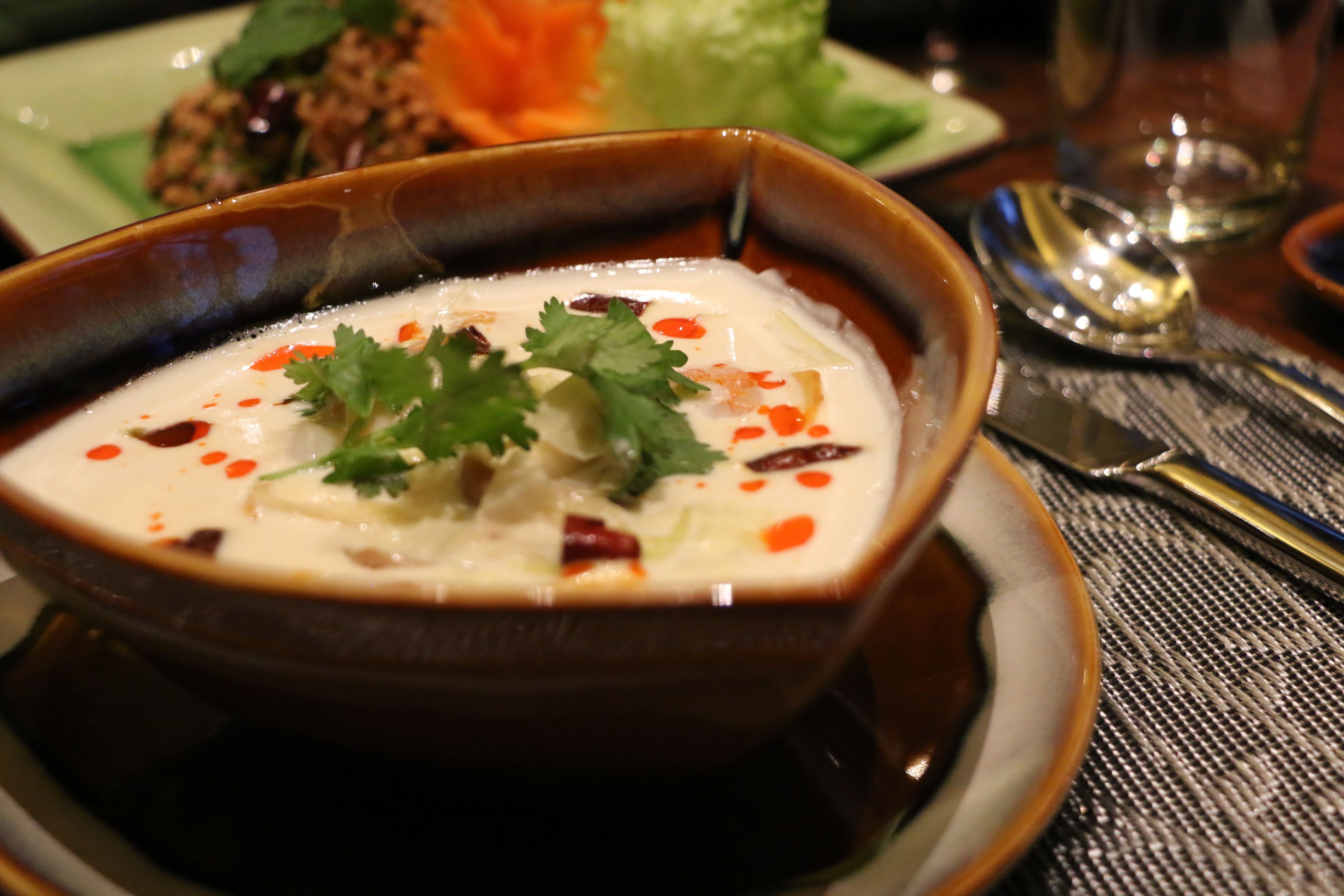 A bowl of soup garnished with cilantro and chili flakes, served on a ceramic plate.