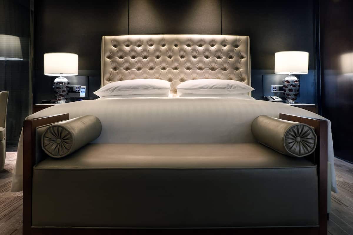 Una cama grande con cabecera capitonada, dos mesitas de noche con lámparas y estructura de madera.