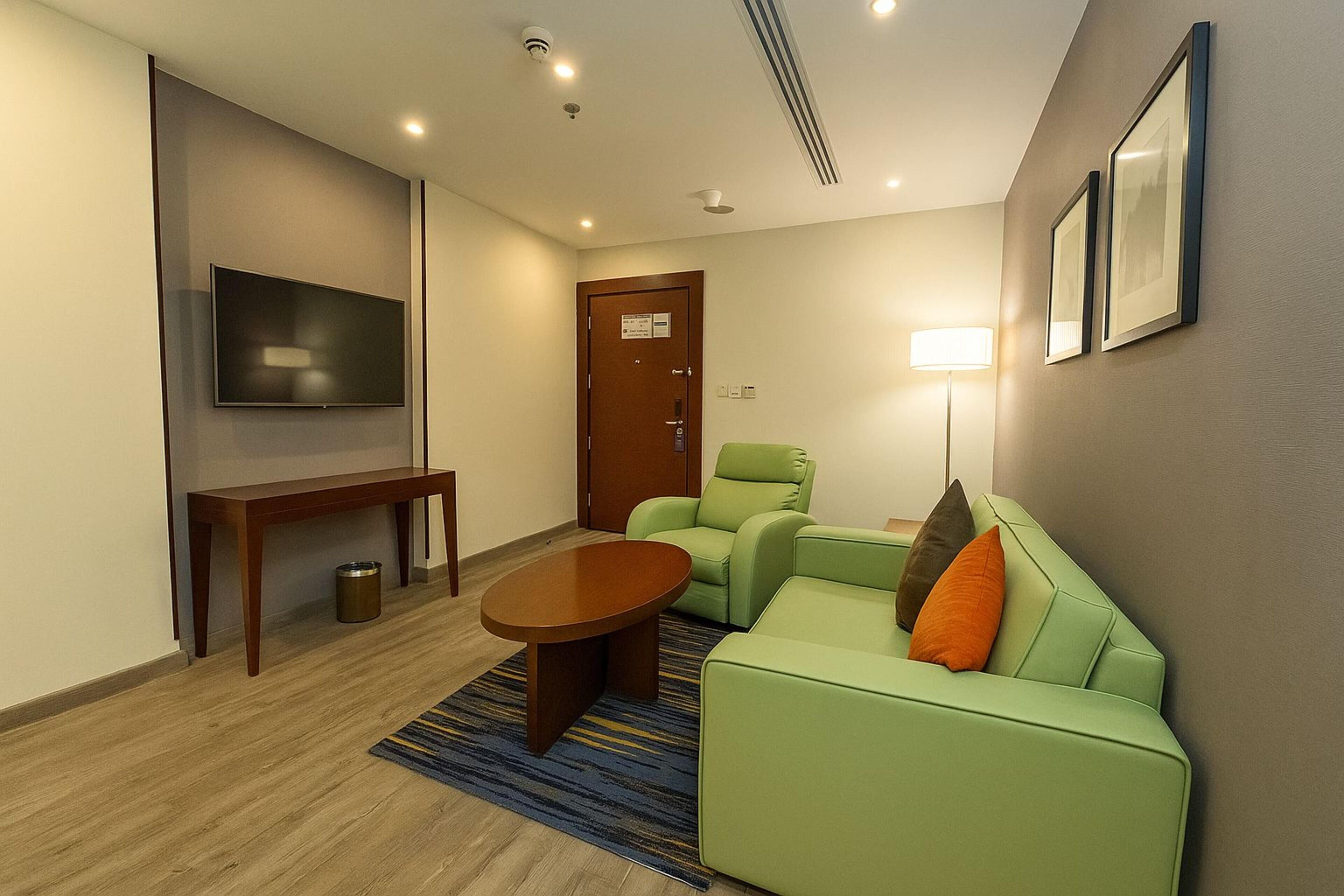 Een moderne woonkamer met een groene bank, een houten salontafel, een flatscreen televisie en een lamp.