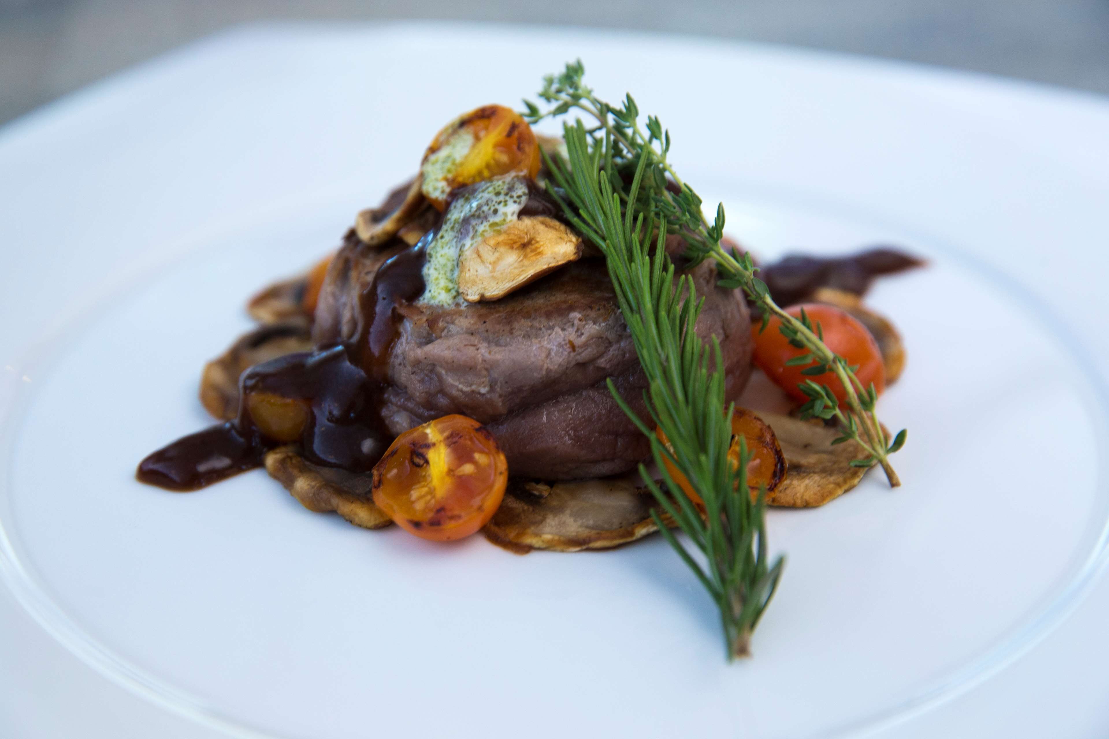 A plate with a steak, mushrooms, and a sprig of rosemary.