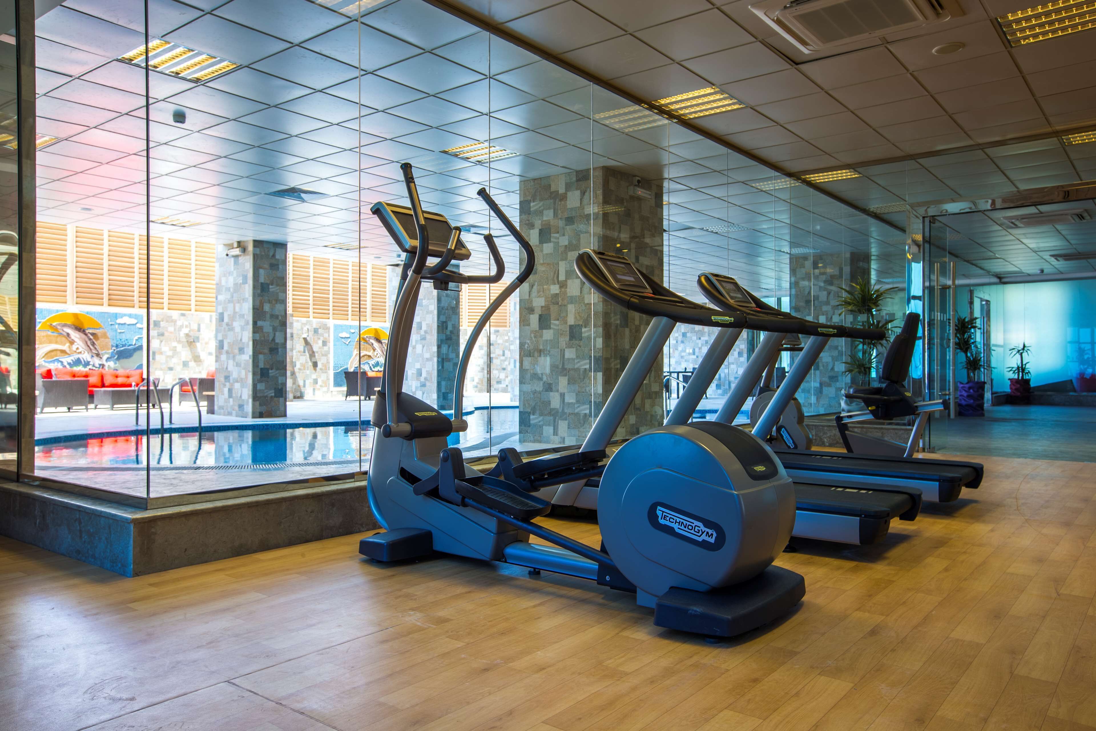 A gym with cardio machines, a glass wall, and a view of outdoor seating.
