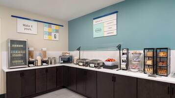 A breakfast bar with a refrigerator, coffee machine, and various food items.