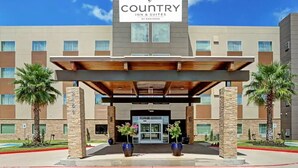 Edificio de Country Inn & Suites con diseño moderno, que cuenta con un acceso cubierto, palmeras y un cielo despejado.