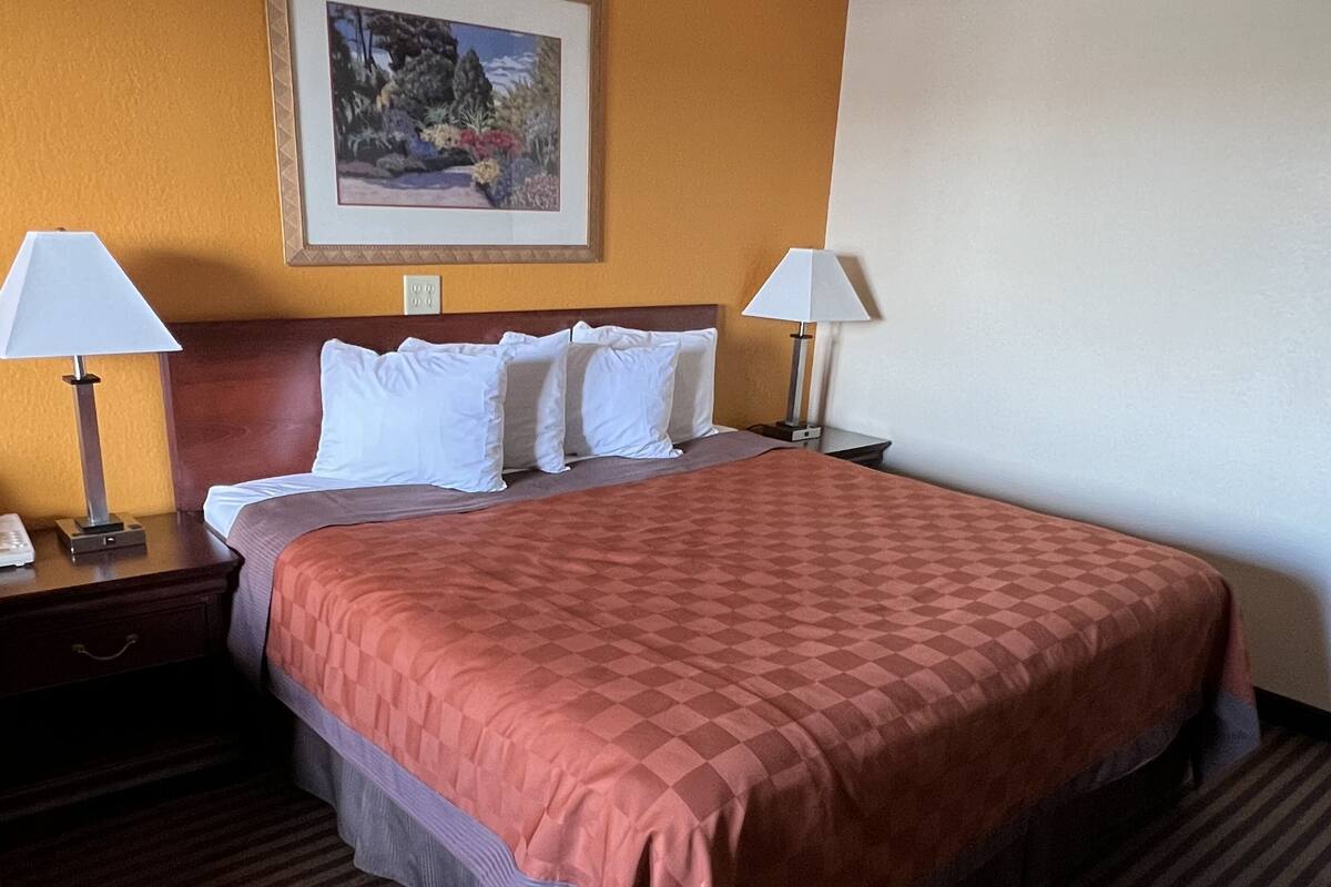 A hotel room with a large bed, two bedside tables with lamps, a framed picture on the wall, and a carpeted floor.