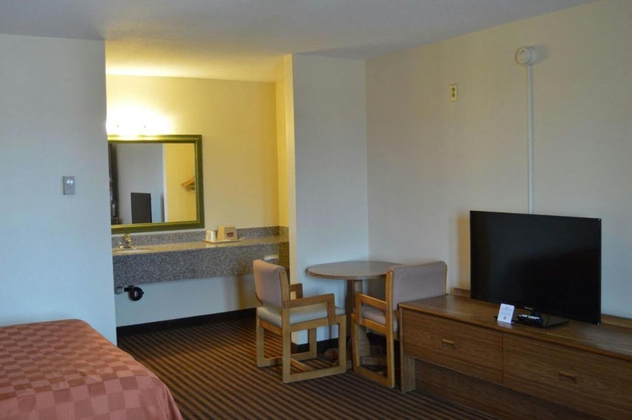 Habitación de hotel con una cama, un escritorio pequeño con televisor, una silla y un espejo.