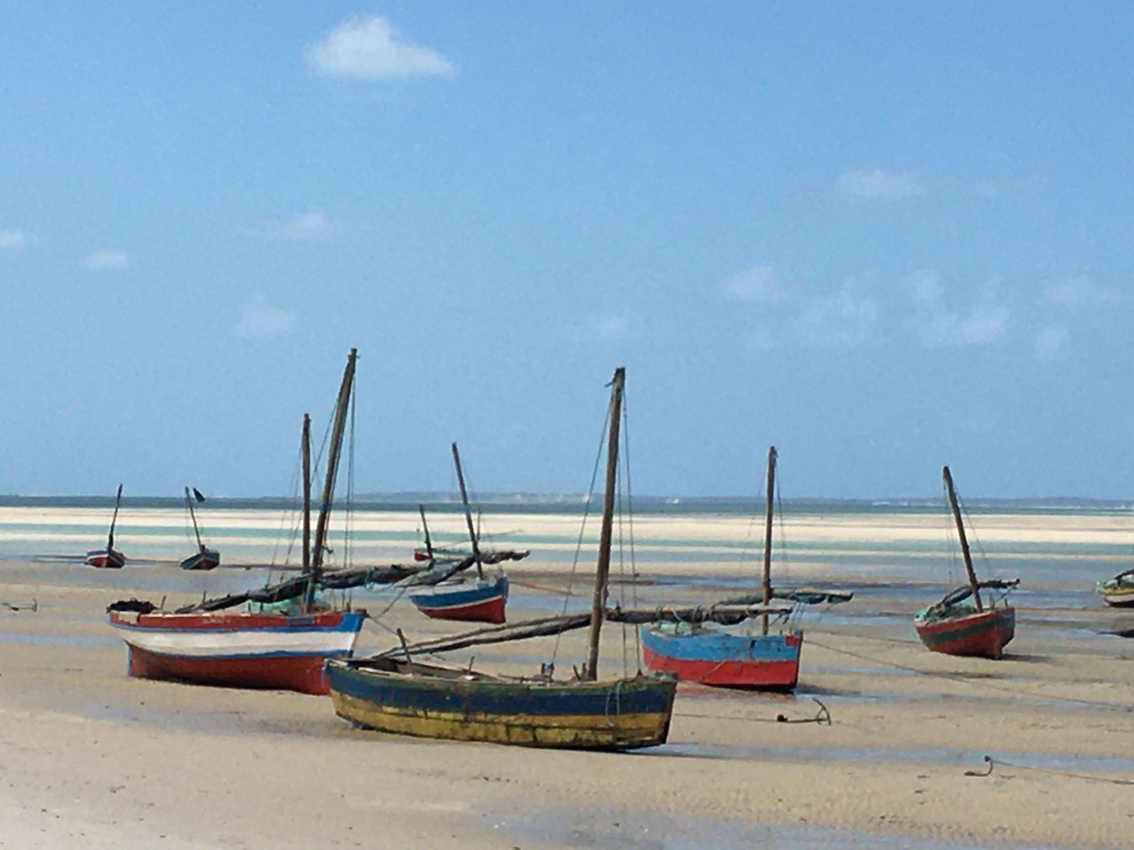 Several boats anchored on a sandy beach with a clear sky.