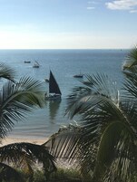 Paisaje costero con barcos en el agua, palmeras y cielo despejado.