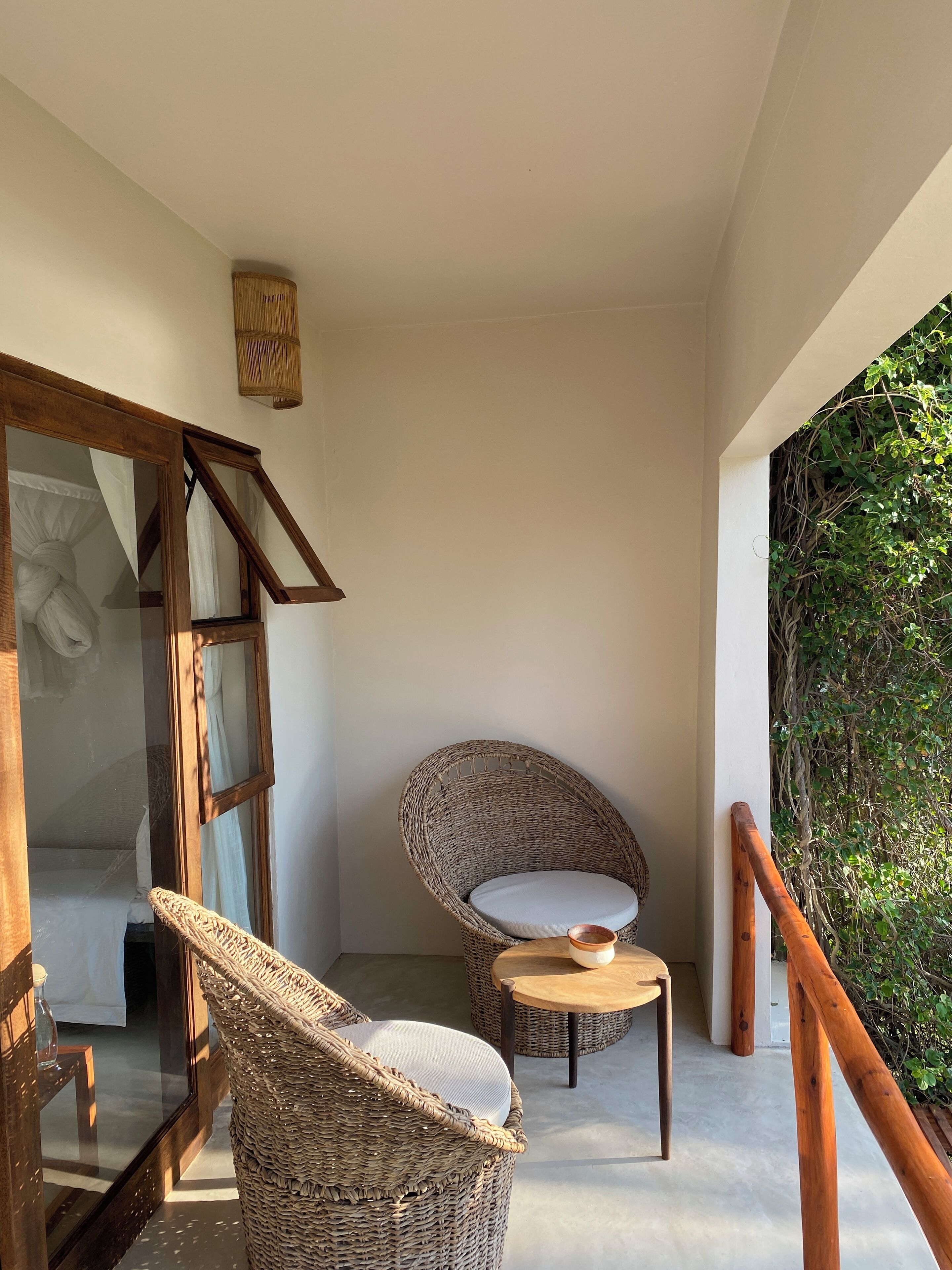 A balcony with wicker chairs, a wooden table, and a view of greenery.