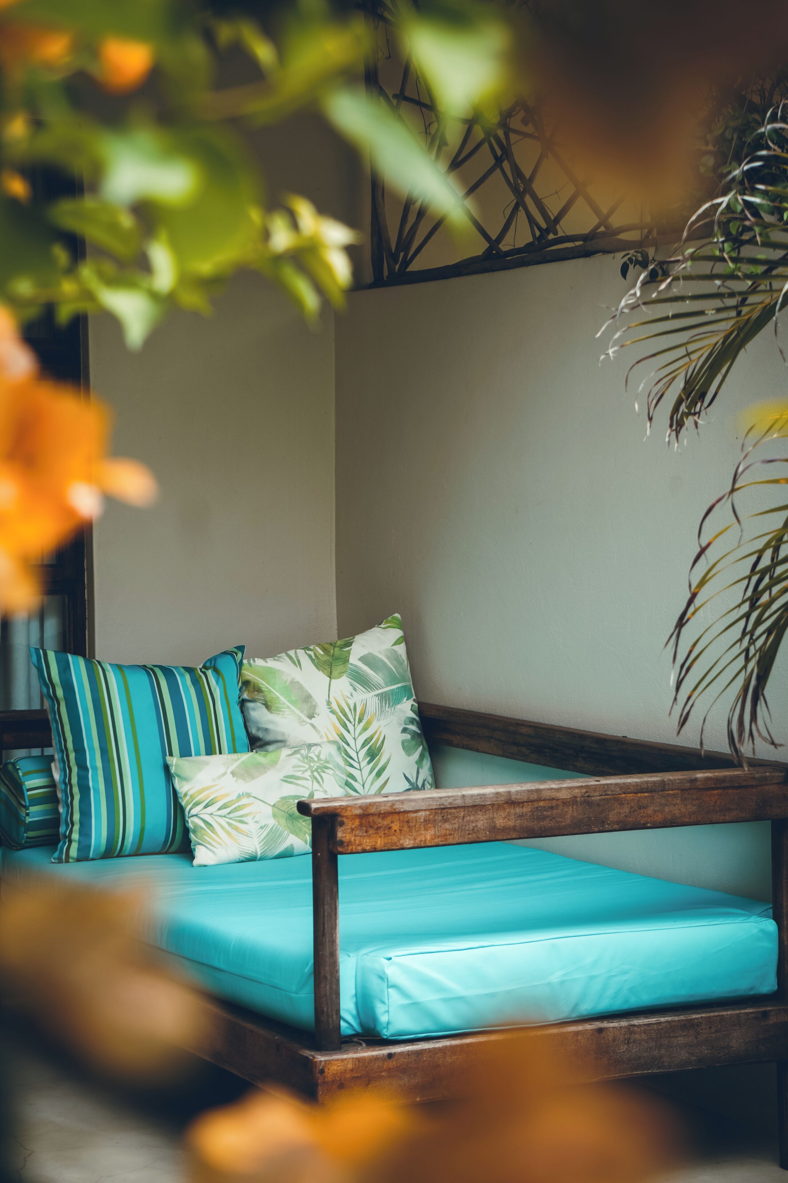 A cozy room with a wooden bench, teal cushions, and a leafy patterned pillow.