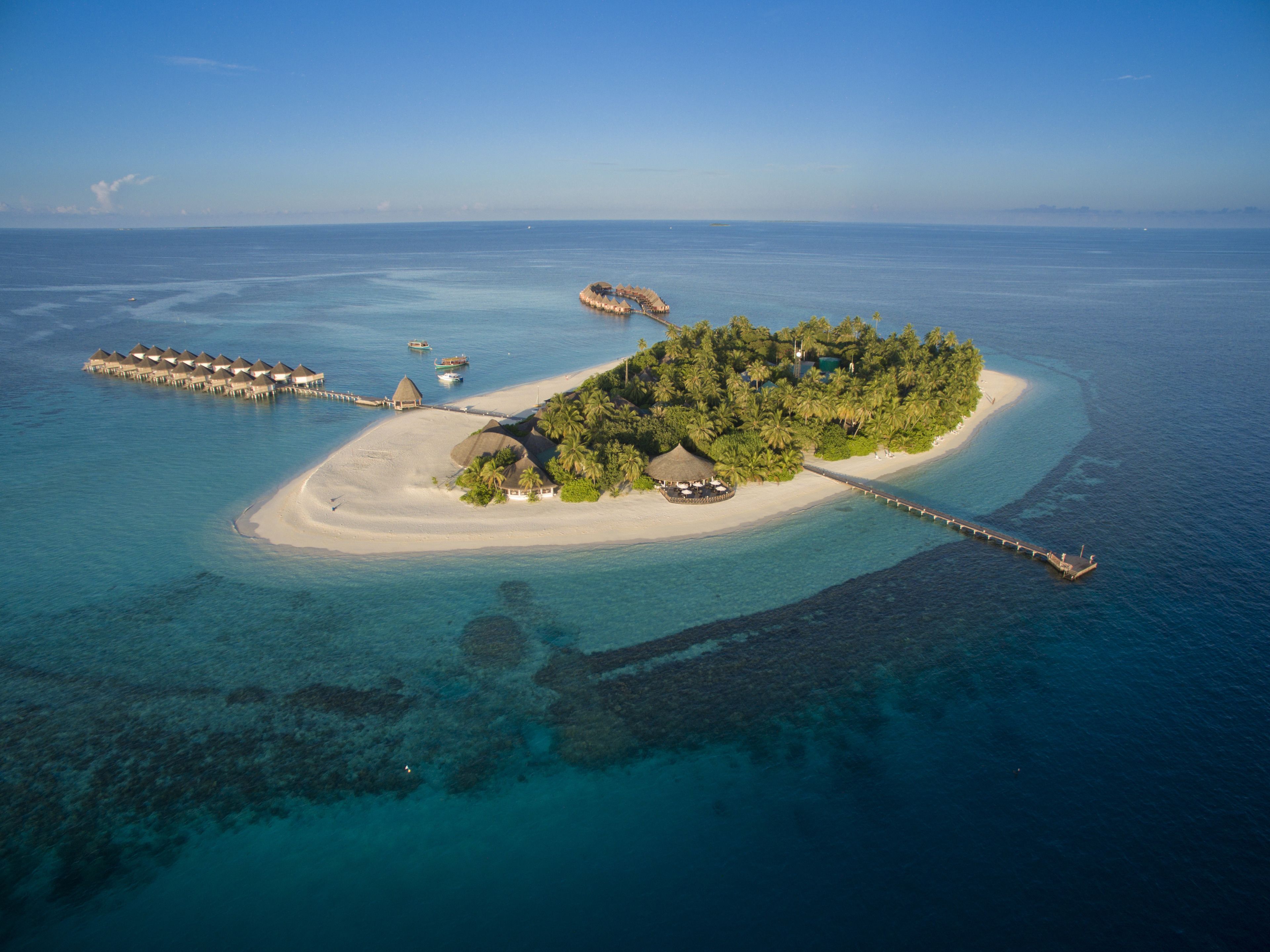 An aerial view of a tropical island with overwater bungalows, a beach, and a pier.