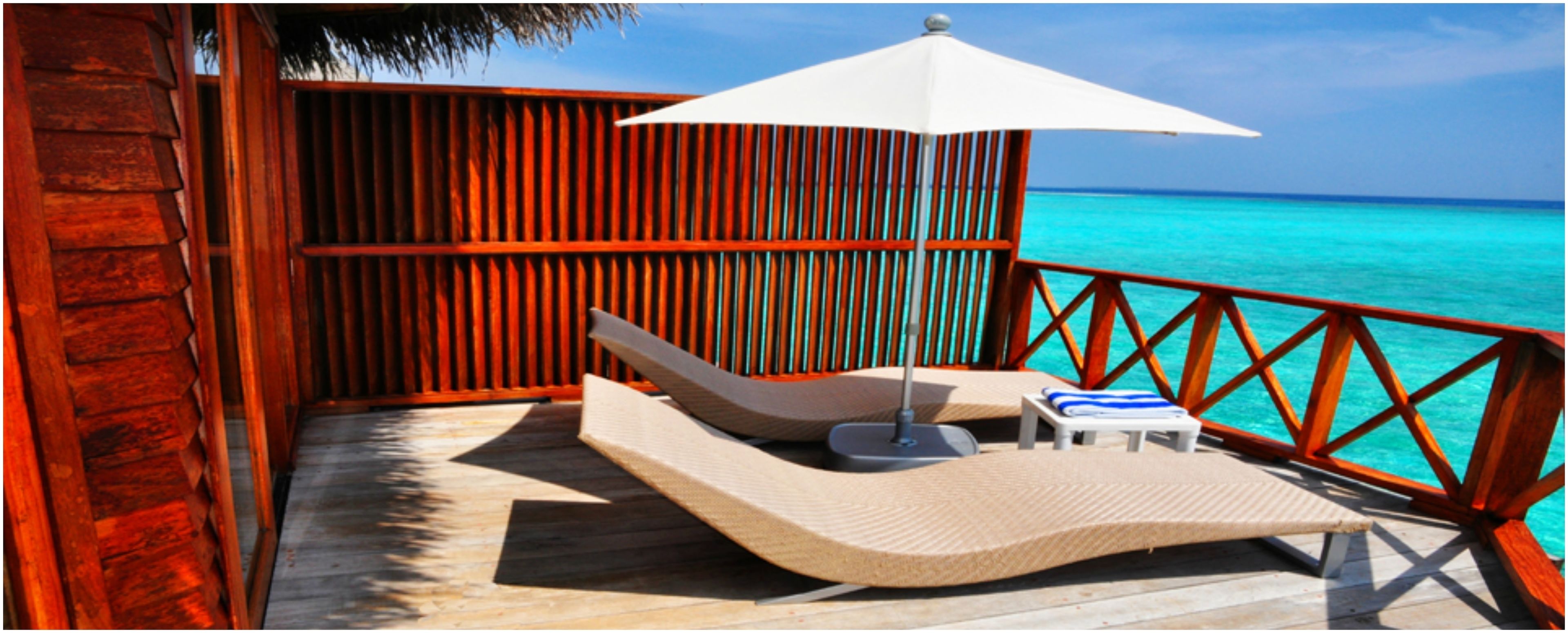 A wooden deck with a lounge chair and a small table, overlooking turquoise waters.