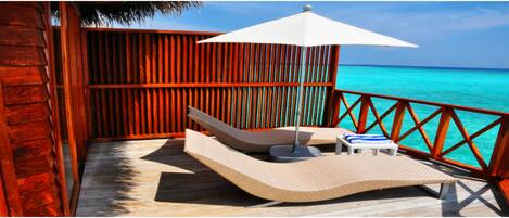 A wooden deck with a lounge chair and a small table, overlooking turquoise waters.