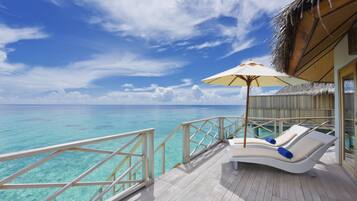 A wooden deck with a white lounge chair and an umbrella, overlooking turquoise waters and a clear sky.