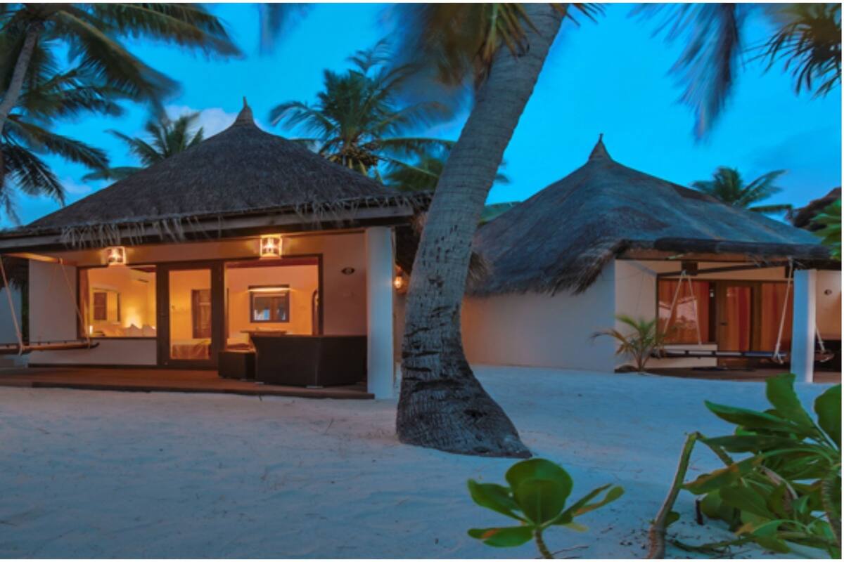 A beachfront resort with thatched-roof overwater bungalows, a sandy beach, and palm trees.