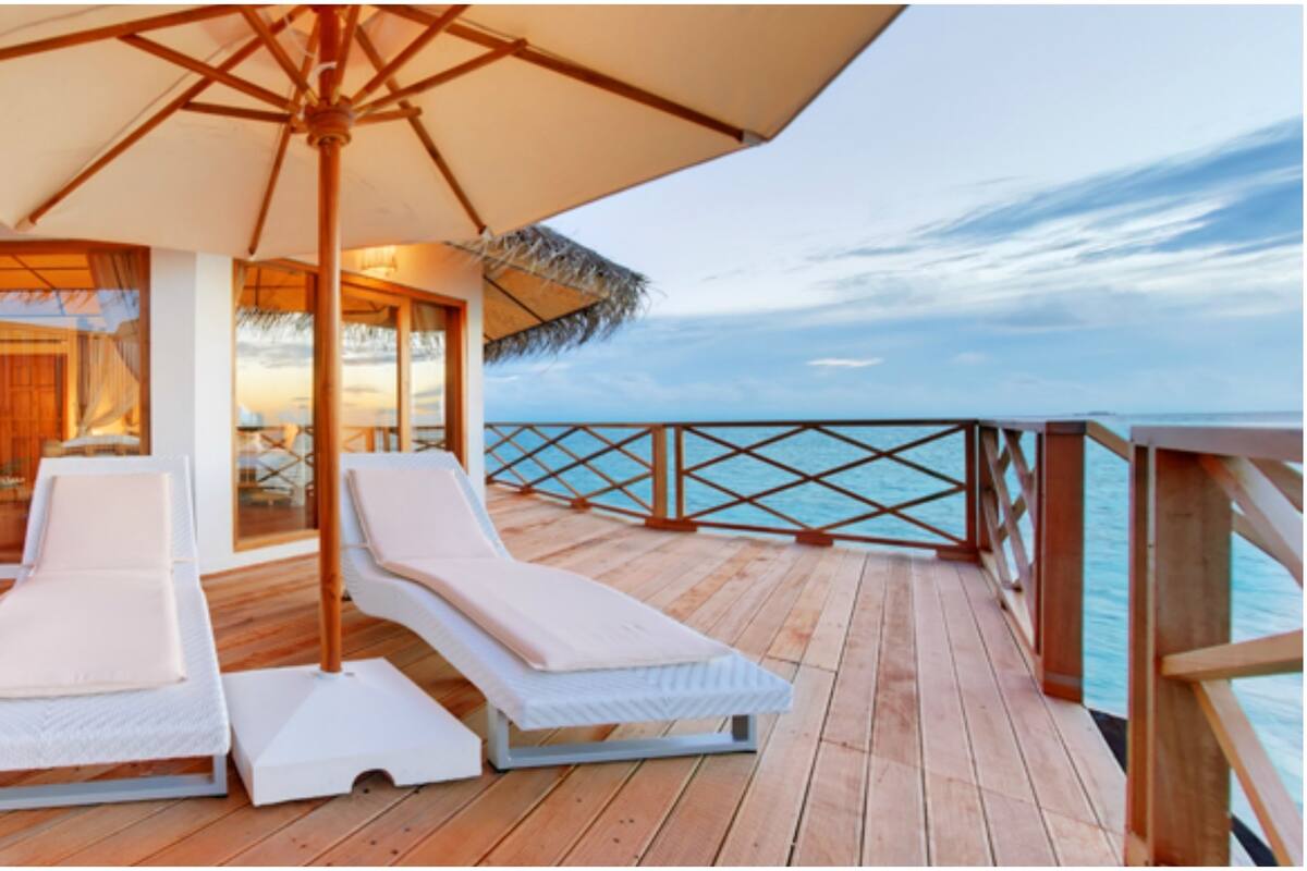 A wooden deck with two white lounge chairs and a large umbrella, overlooking a body of water.