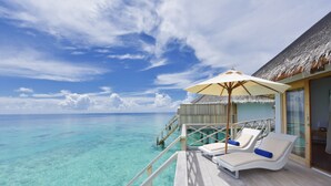 Una terraza con dos sillones de descanso y un parasol con vistas a aguas turquesas.