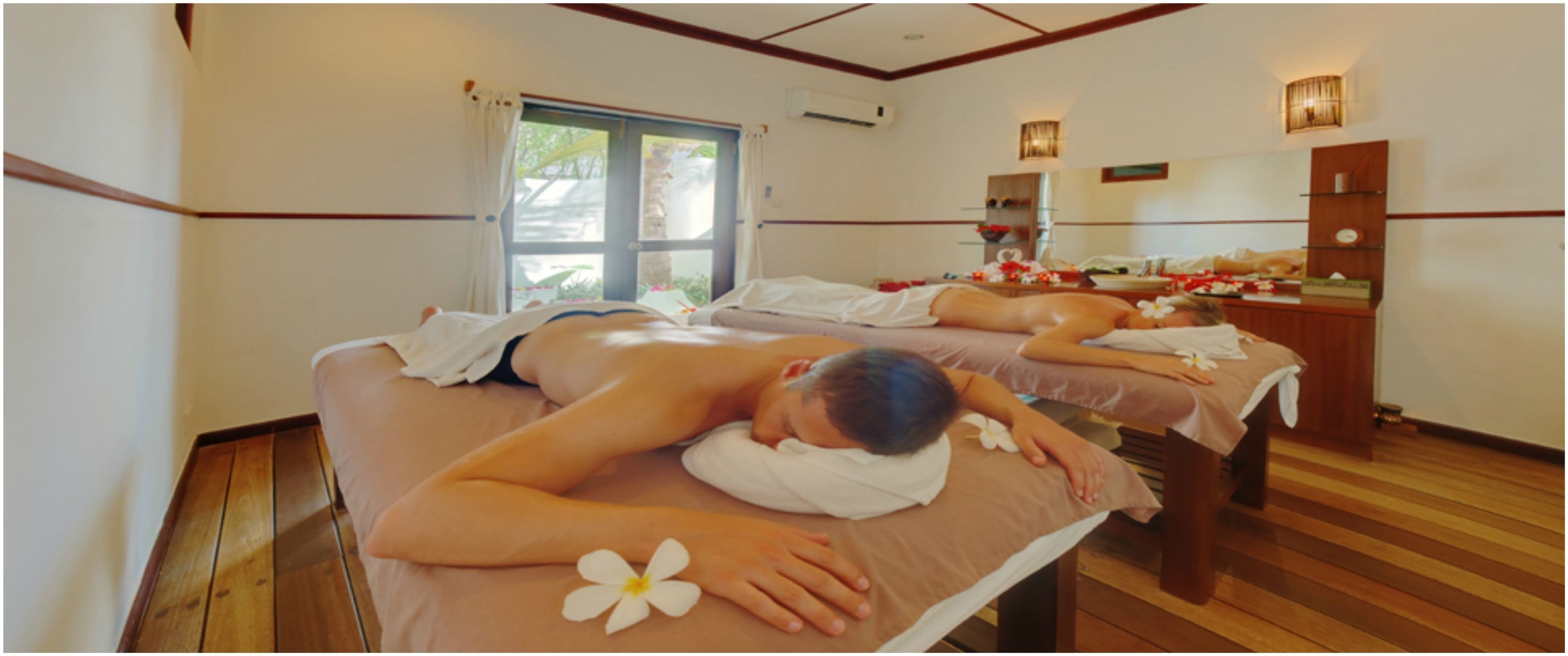 Une pièce comprenant deux tables de massage, un plancher en bois, une fenêtre avec des rideaux et un miroir au mur.