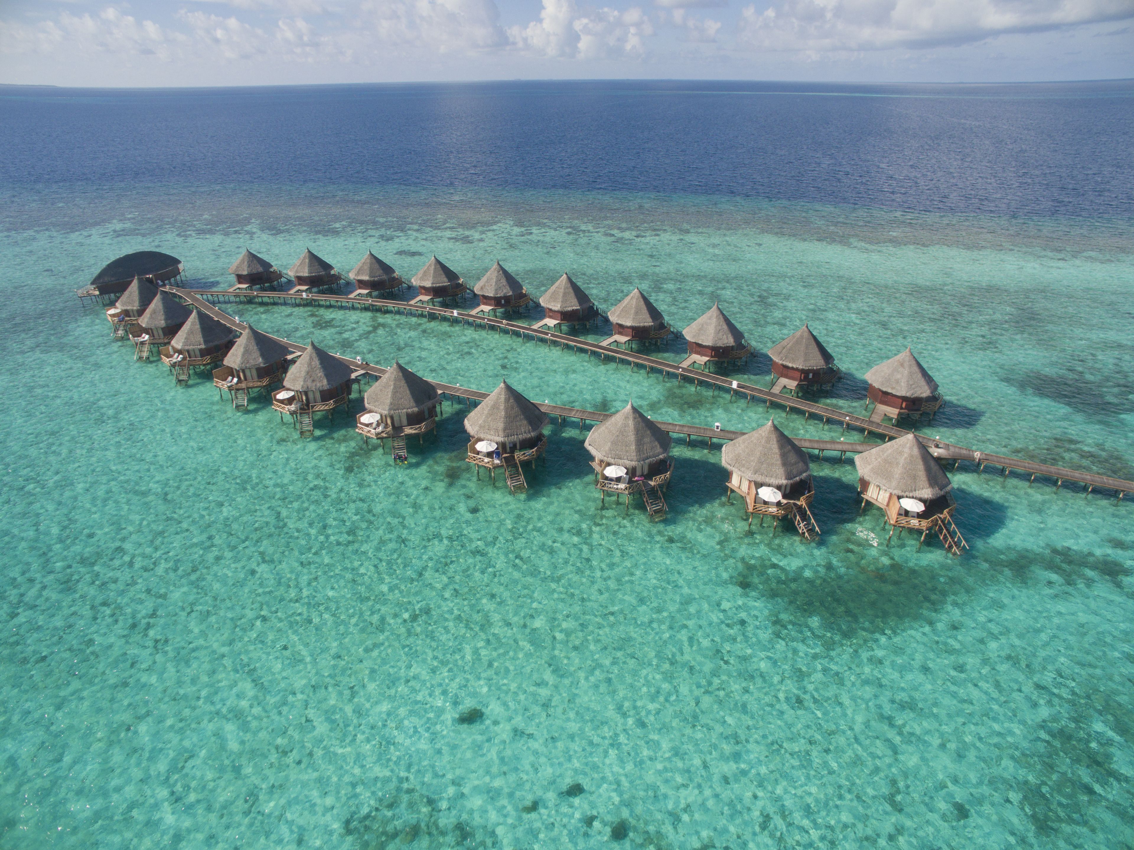 An aerial view of overwater bungalows connected by walkways over clear turquoise waters.