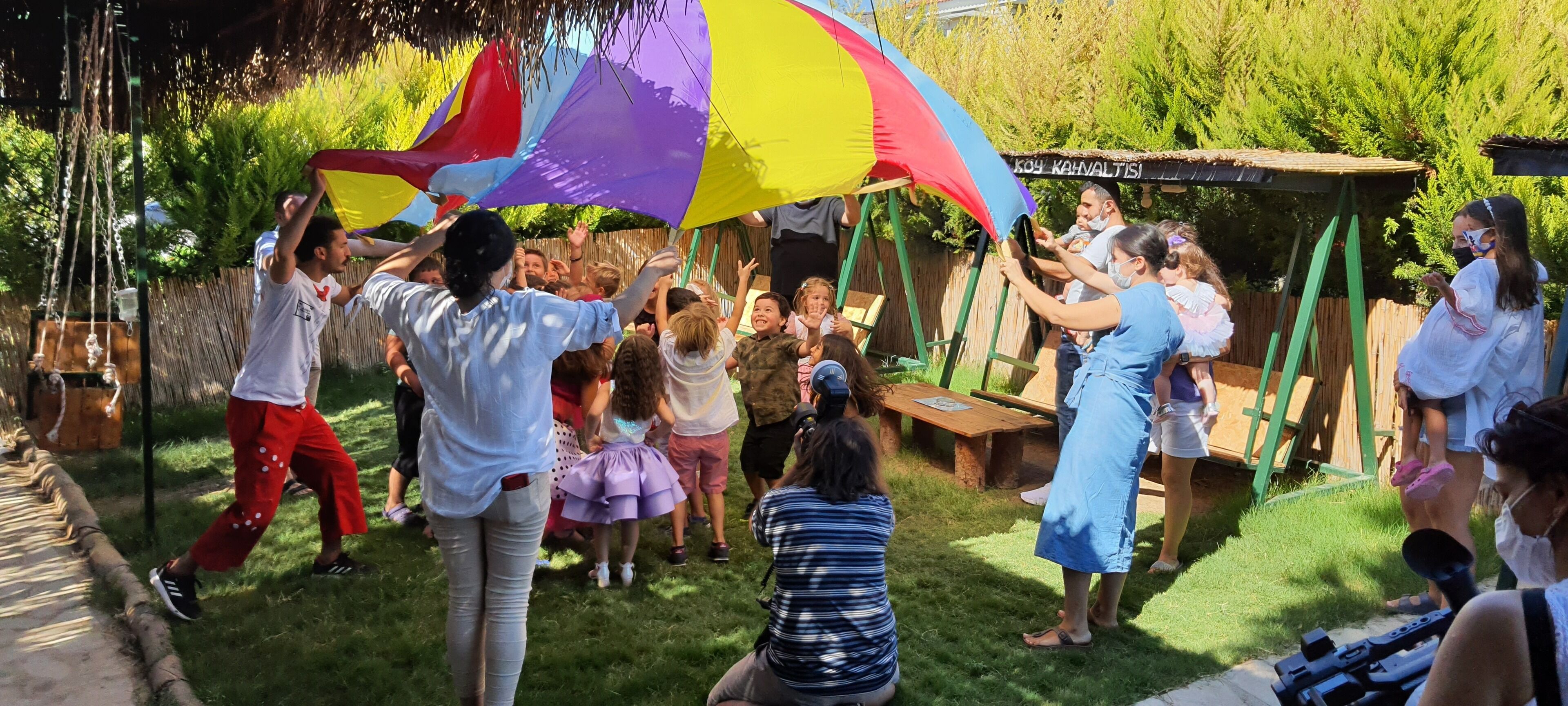 A group of people gathered outdoors, some holding a colorful umbrella.