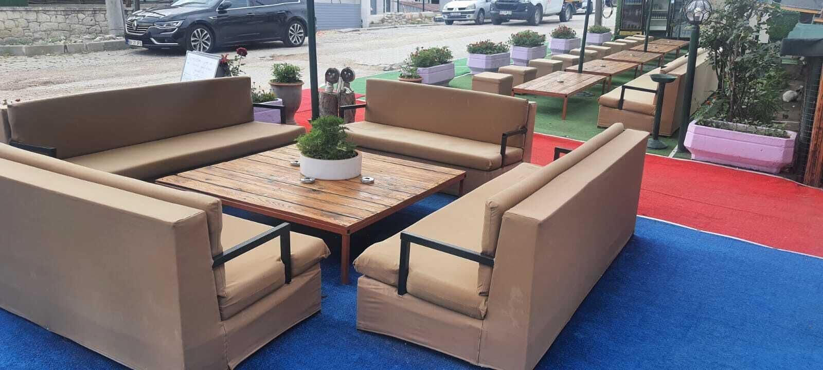 Mobiliario exterior con sillas acolchadas y una mesa de madera, rodeado de plantas en macetas.