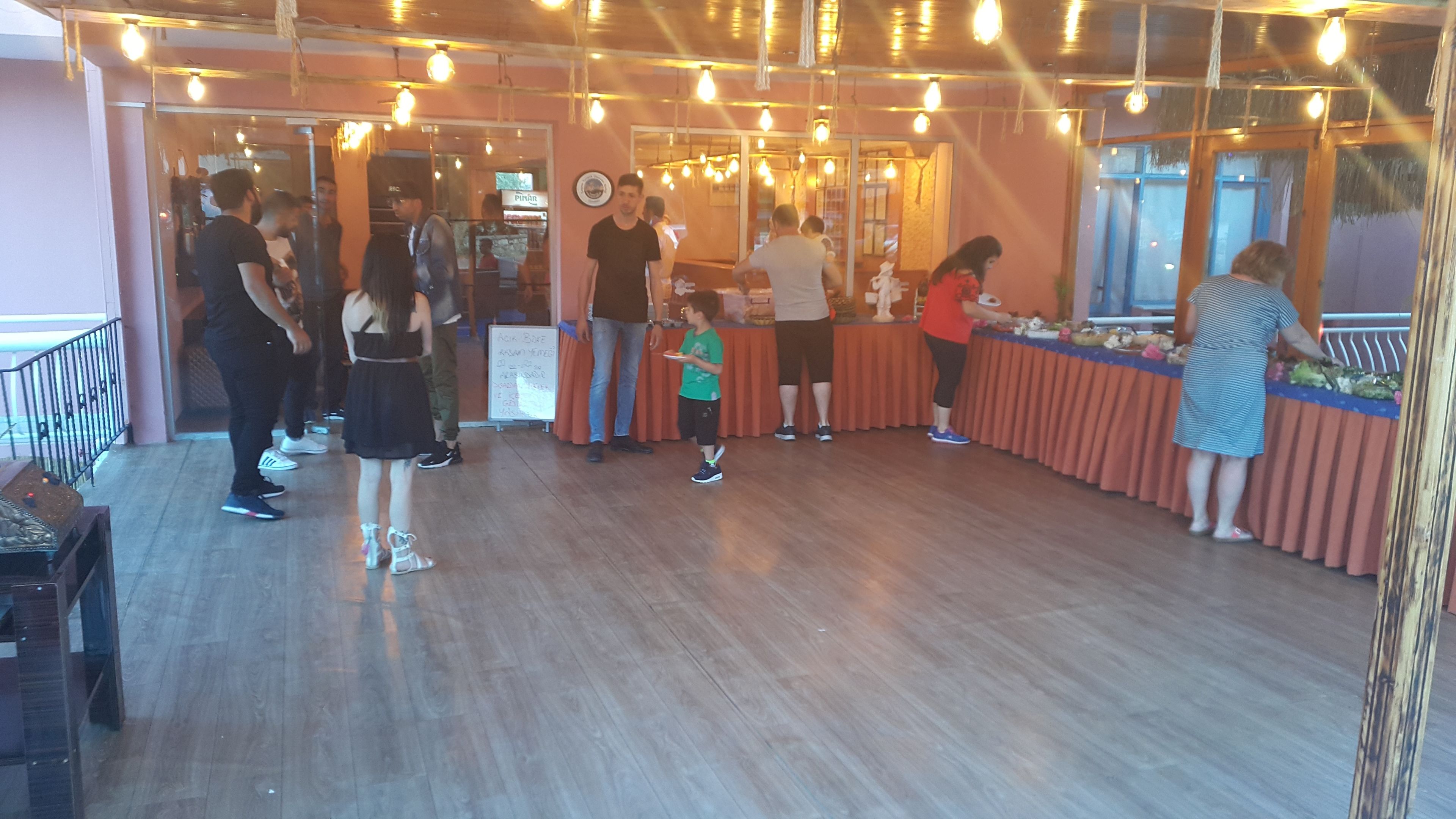Interior de restaurante com piso de madeira, lâmpadas pendentes e balcão com alimentos.