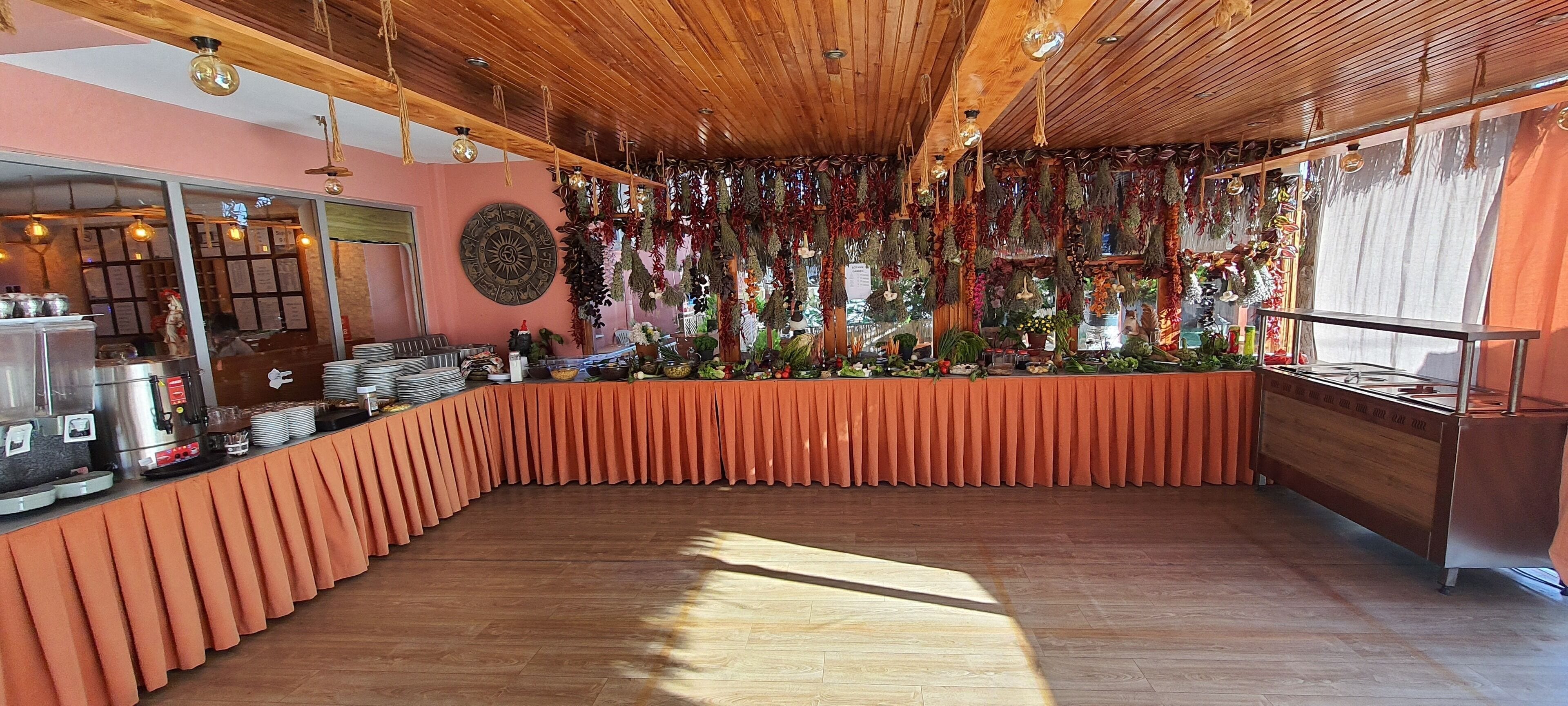 A restaurant with a wooden ceiling, a counter with a pink tablecloth, and hanging plants.