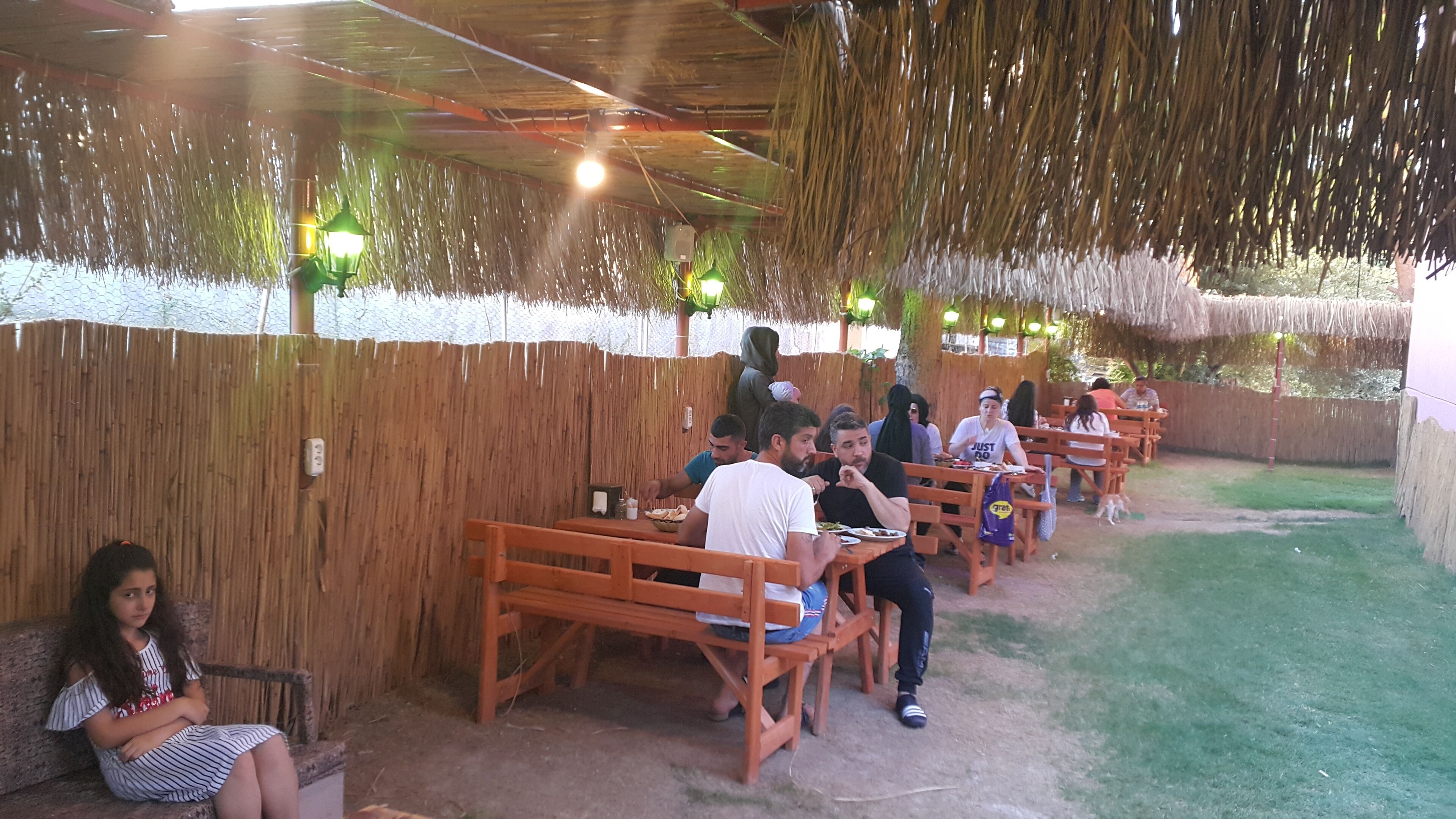 An outdoor dining area with wooden benches and tables, a bamboo fence, and hanging lights.