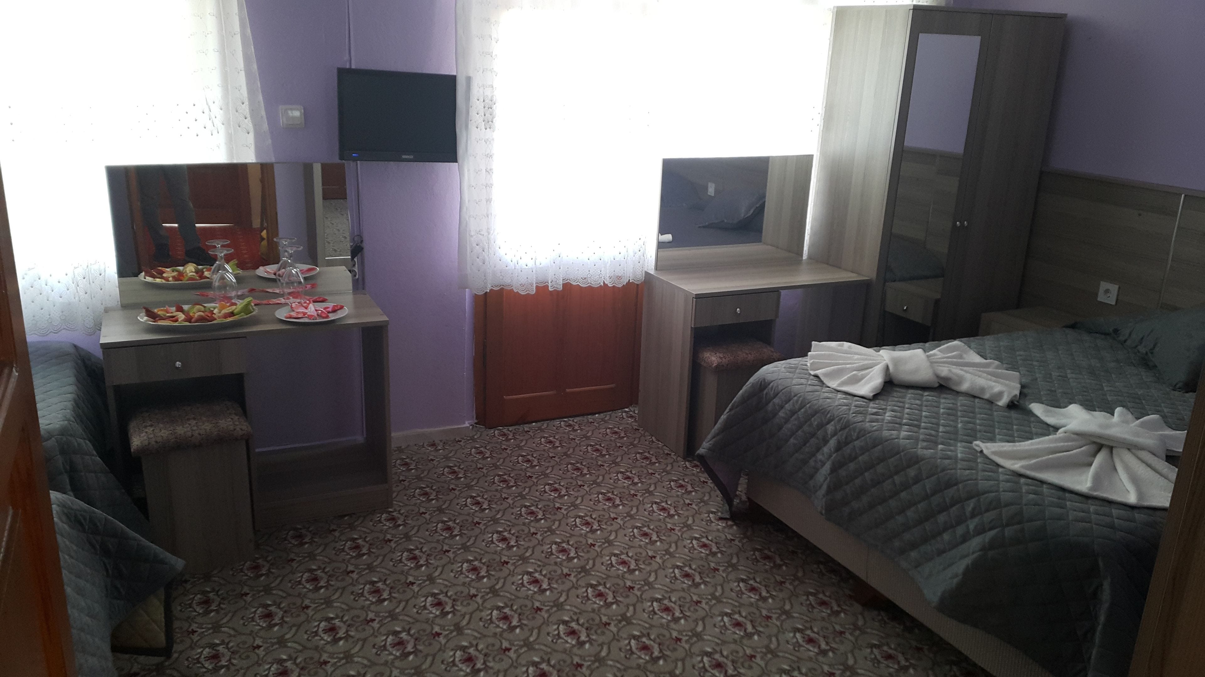 Habitación de hotel con cama, escritorio, televisor de pantalla plana, espejo y ventana con cortinas.